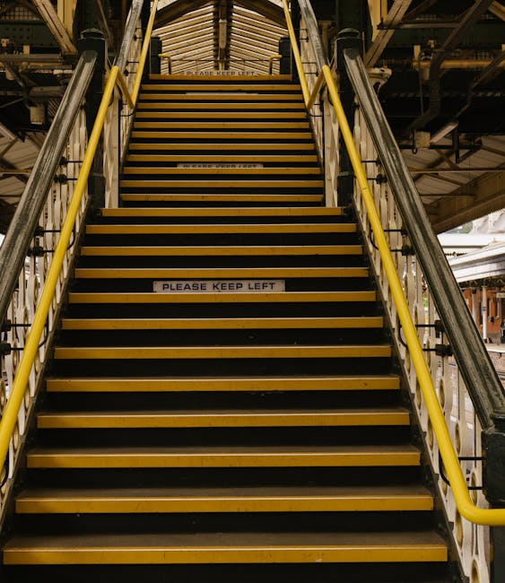 A set of concrete stairs with metal railings leading up to an underground or elevated area within a public transport station or multi-level building. The stairs have black anti-slip treads on each ste